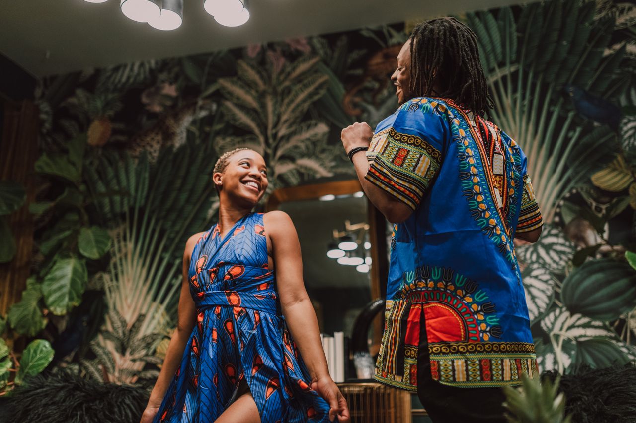 Happy couple celebrating in colorful African attire, embracing culture and tradition indoors.